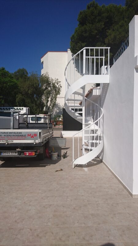 Escalera de caracol fabricada en metal lacado blanco instalada en el exterior de una vivienda.