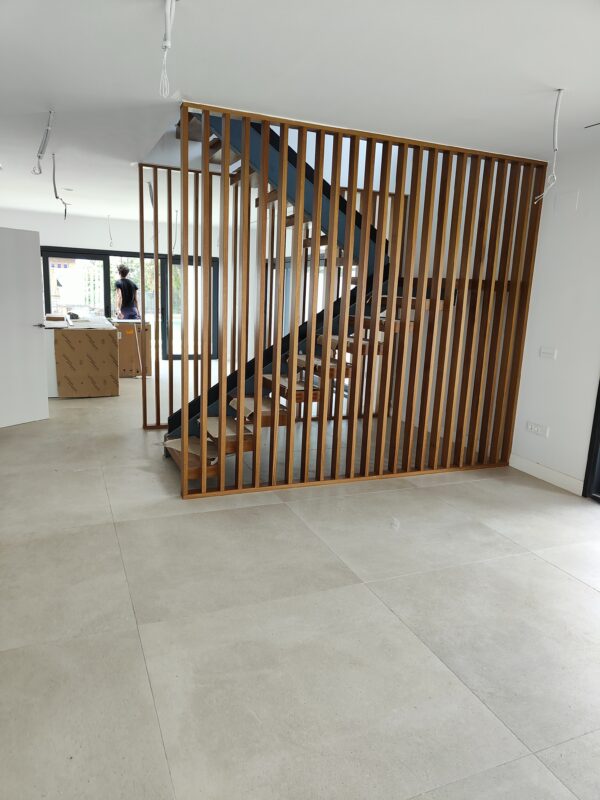 Escalera moderna fabricada en carpintería metálica con peldaños de madera y cerramiento decorativo de listones verticales.